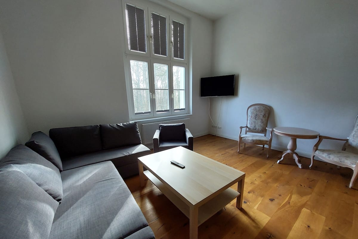 A living room with a sectional sofa, a coffee table, a TV mounted on the wall, and a small round table.