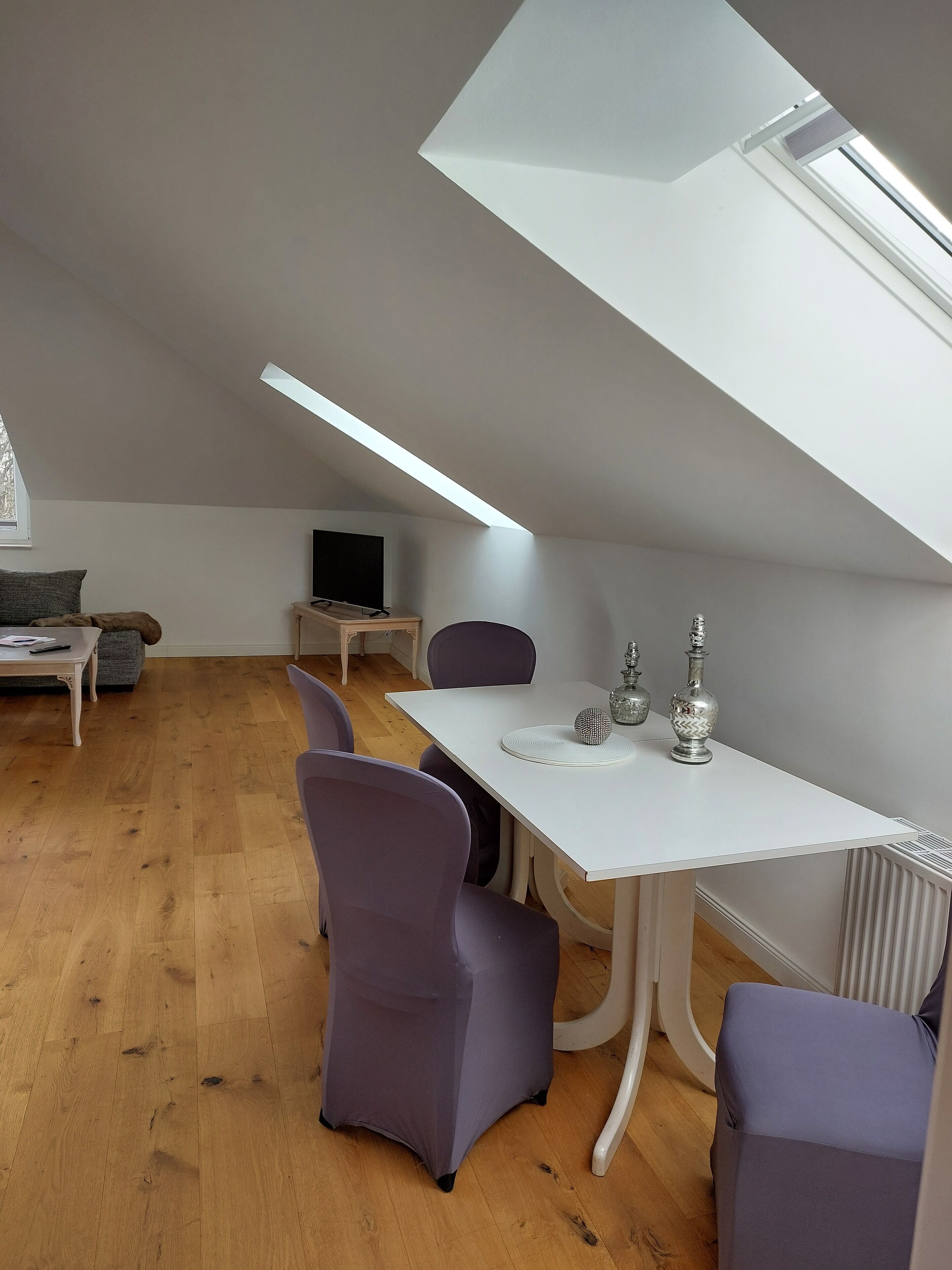 A modern loft-style room with a dining table, purple chairs, a TV, and a skylight.