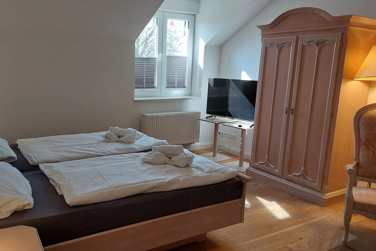 A bedroom with two beds, a TV, a wardrobe, and a desk with a lamp.
