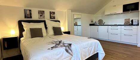 Ein Schlafzimmer mit einem großen Bett, einem Nachttisch, einem Wand-Fernseher und einer Küchenzeile mit Schränken und einer Mikrowelle.