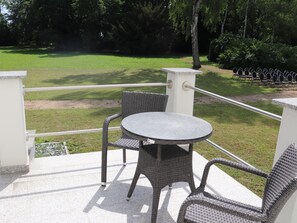 A balcony with a round table and wicker chairs, overlooking a grassy area with trees and a row of chairs. - Schloss Hohendorf (Gross Mohrdorf)