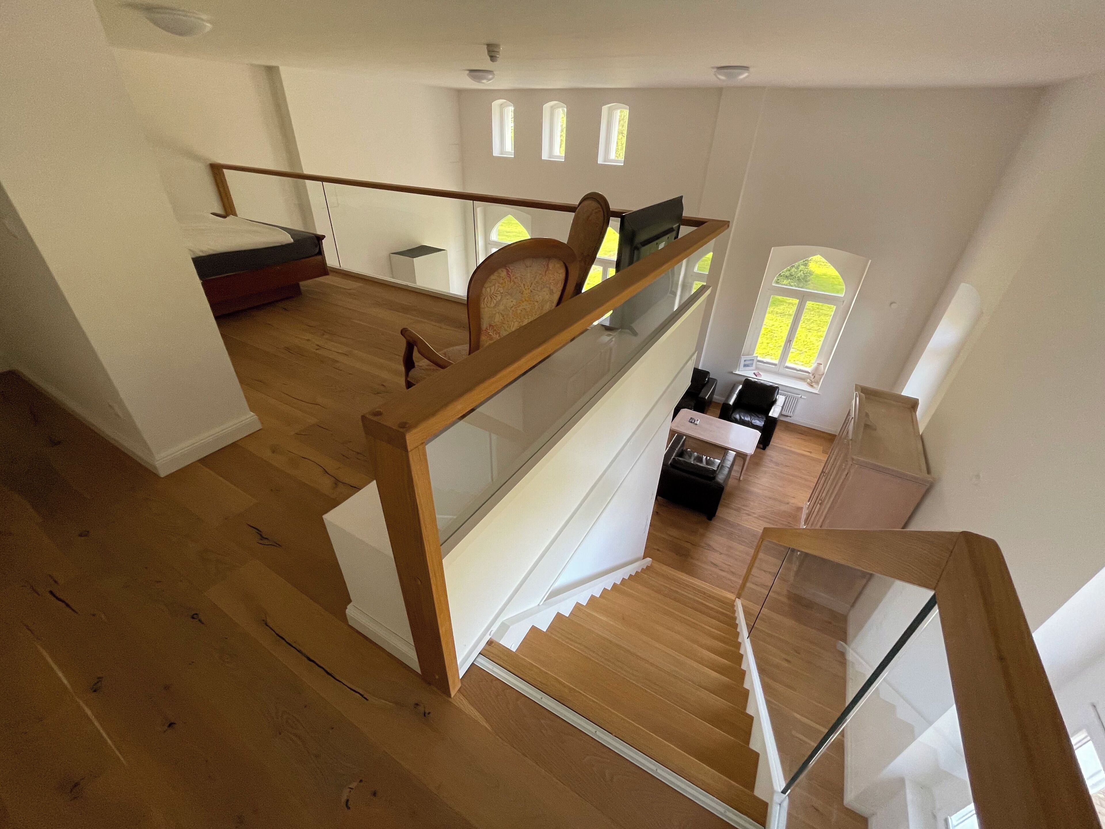 Un vaste espace de vie agrémenté d’un escalier en bois, un coin repas avec une table et des chaises, et une vue sur l’extérieur par une fenêtre.