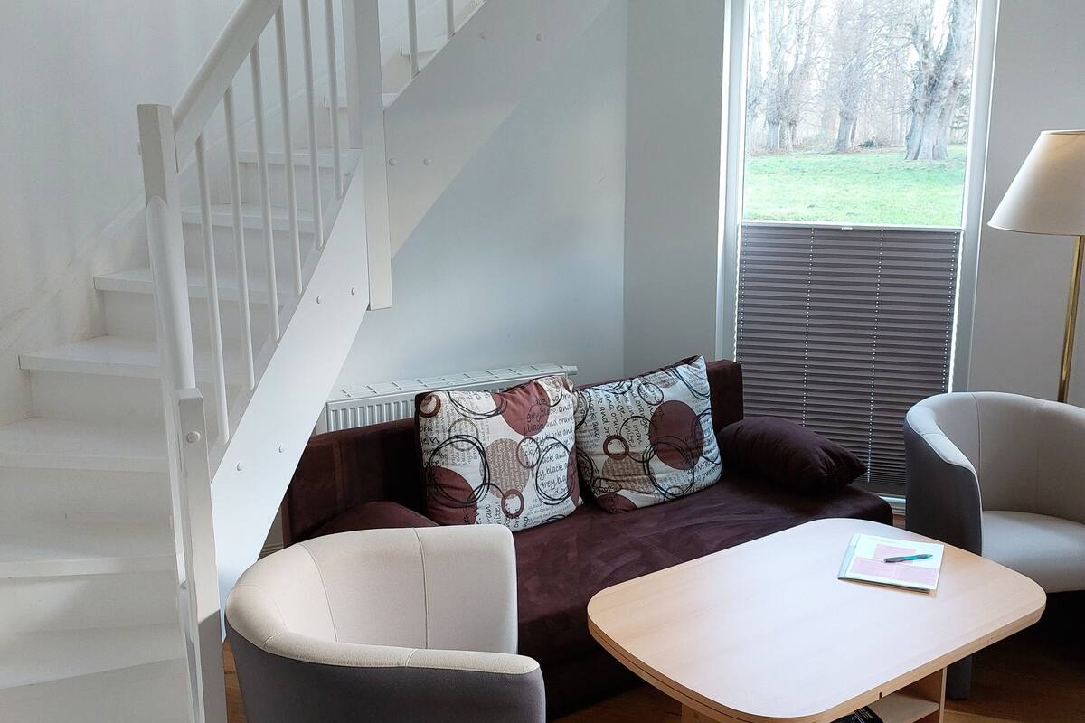 A modern living room with a staircase, a sofa set, a coffee table, and a bookshelf.