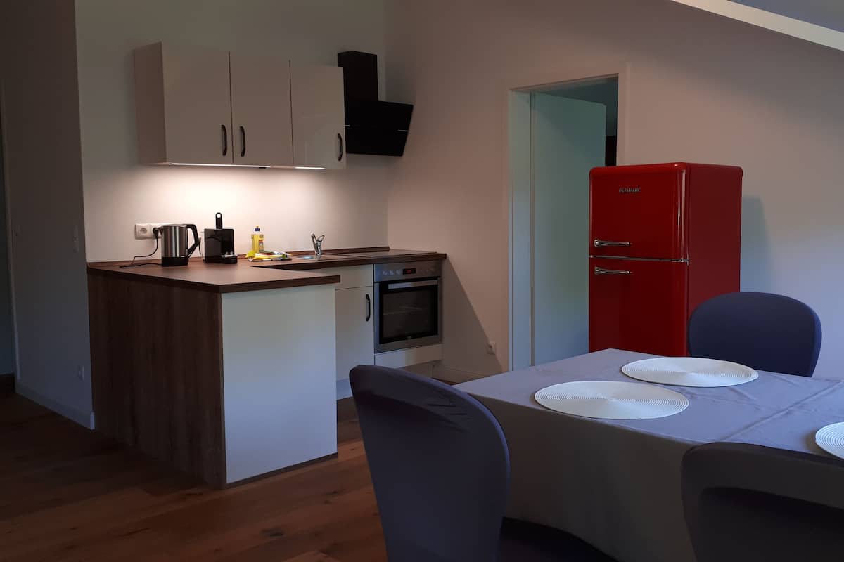A compact kitchen with a built-in oven, a red refrigerator, and a dining area with a table set for four.