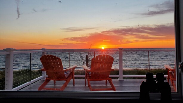 Vista del atardecer desde un balcón con dos sillas Adirondack rojas y un par de binoculares.