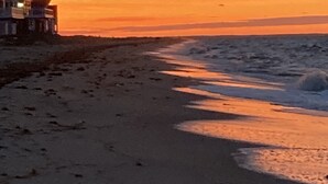 Una playa con una casa a la izquierda, olas acercándose a la orilla y un cielo al atardecer.