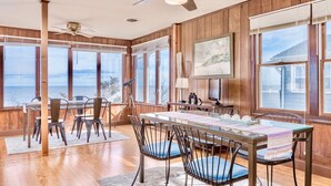 Un comedor amplio con una gran mesa y sillas, paredes de madera y ventanas grandes con vistas al océano.