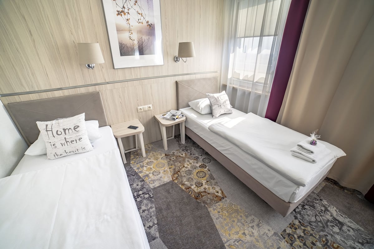 Habitación de hotel con dos camas, una mesita, una lámpara y una ventana con cortinas.