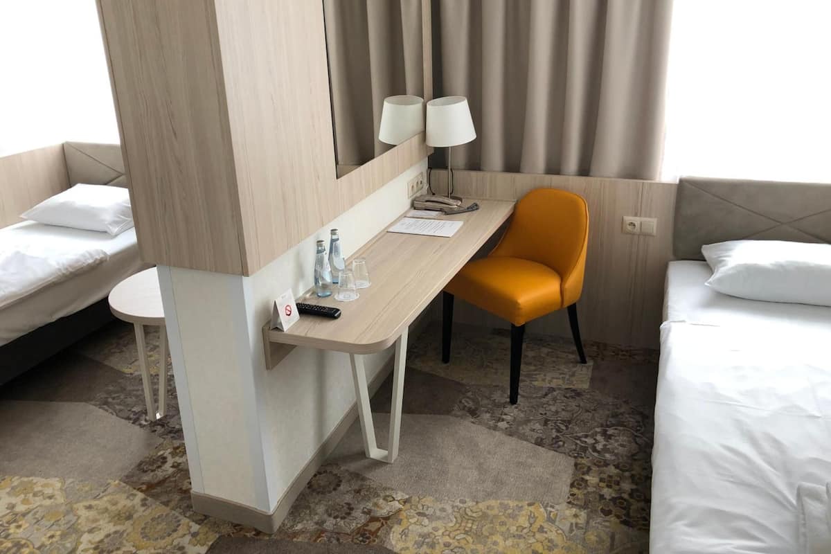 Habitación de hotel con dos camas, un escritorio con una silla, una lámpara y una mesita con un control remoto y una botella de agua.
