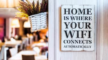A sign that reads "HOME IS WHERE YOUR WIFI CONNECTS AUTOMATICALLY" on a white wooden wall.