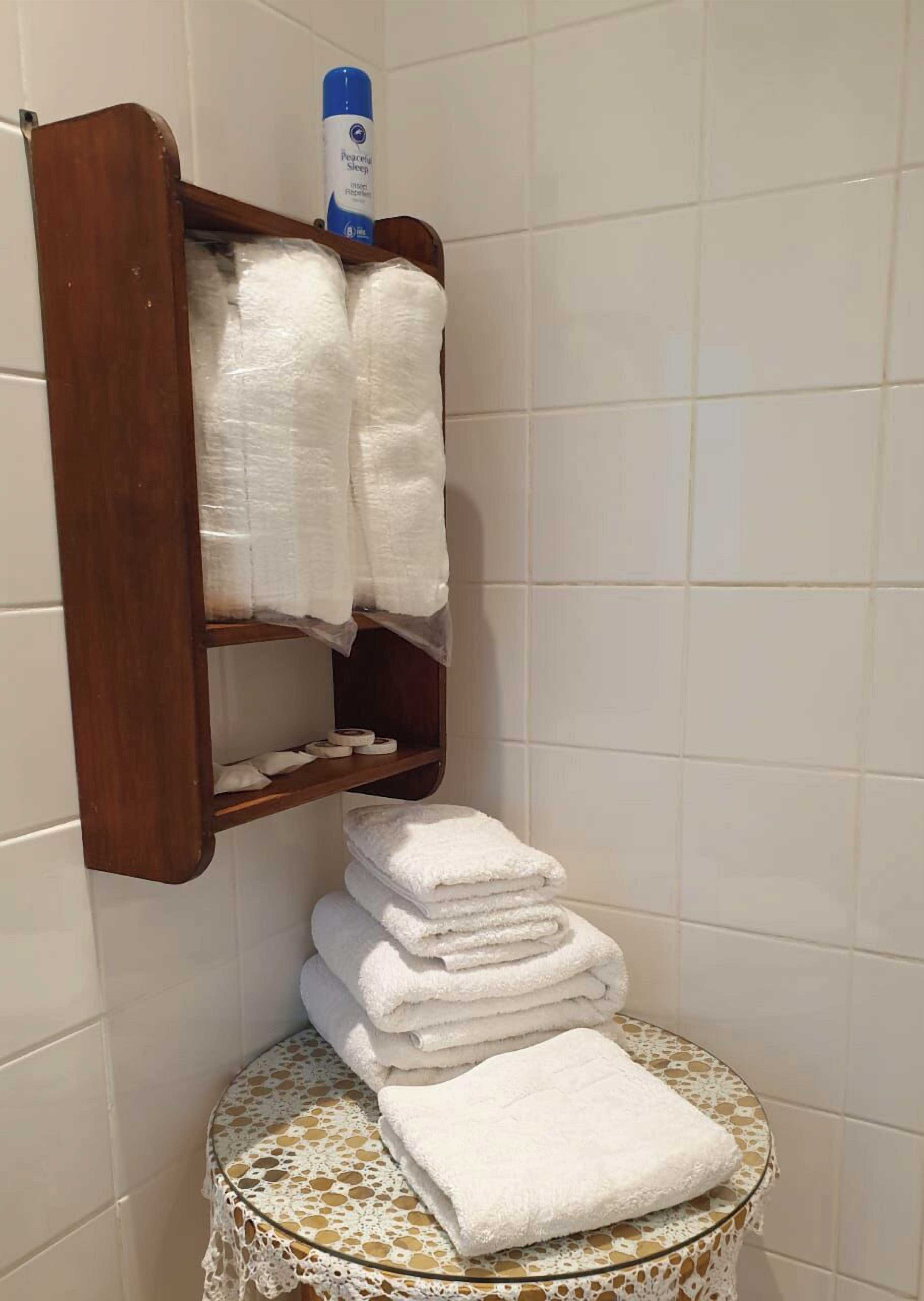 A bathroom with a wooden towel rack holding several folded towels and a bottle of lotion.