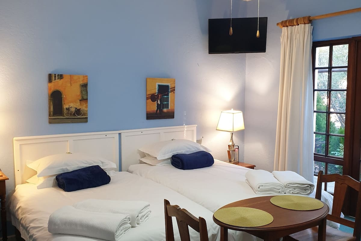 Ein Hotelzimmer mit zwei Betten, einem Deckenventilator, einem an der Wand montierten Fernseher und einem Fenster mit Vorhängen.