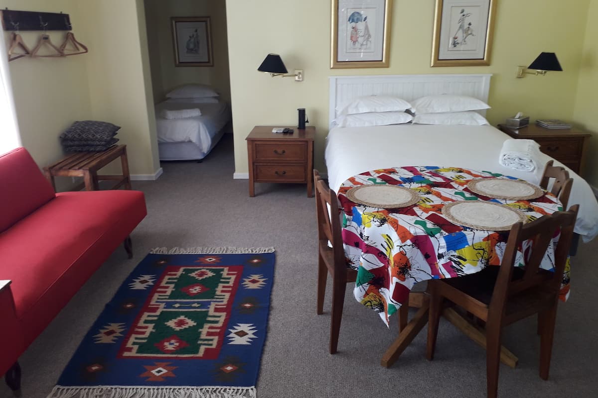 Ein Hotelzimmer mit Bett, einem roten Sofa, einem Esstisch mit Stühlen, einem kleinen Nachttisch und einem Beistelltisch.