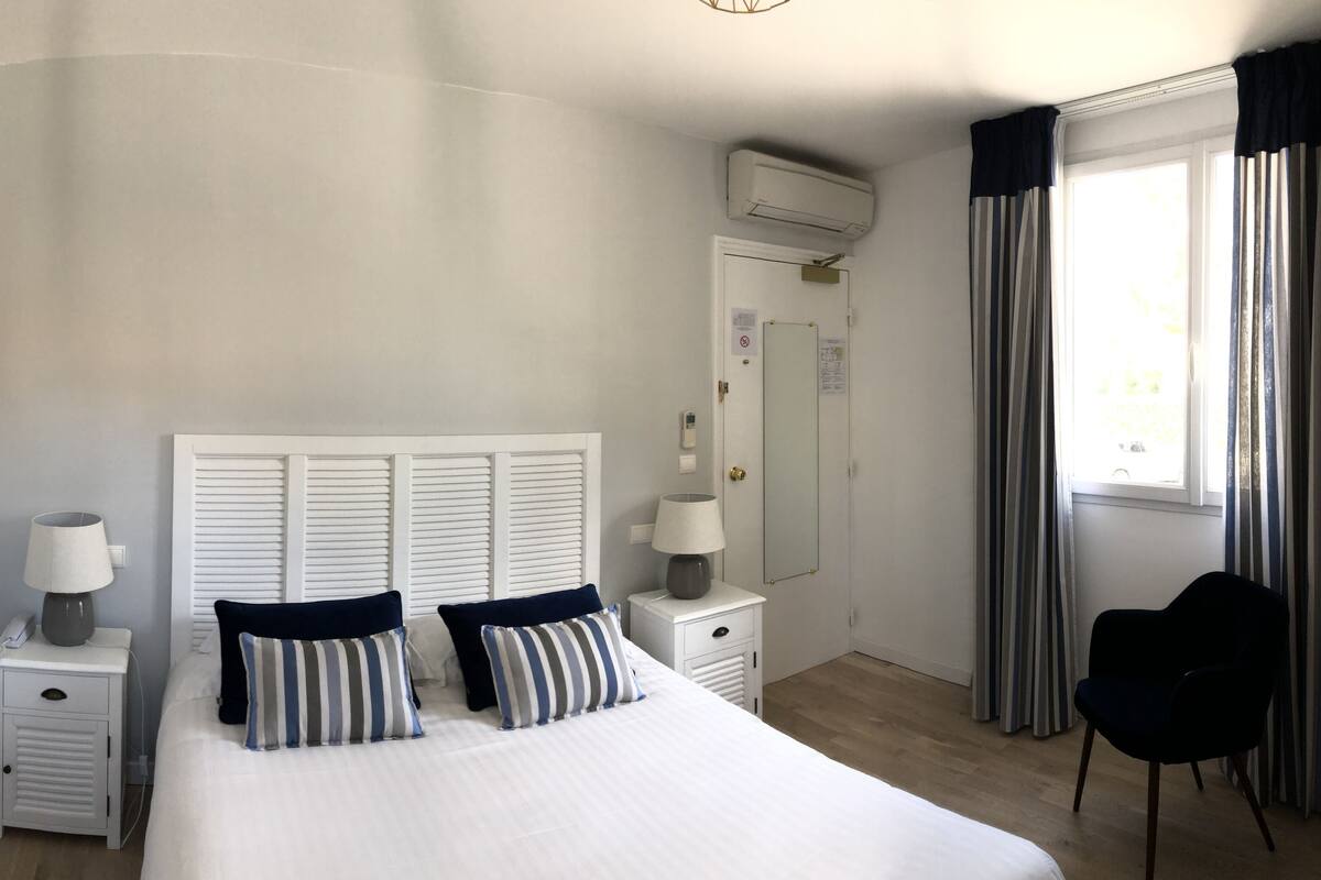 A bedroom with a bed, two bedside tables, a lamp, a chair, and a window with curtains.