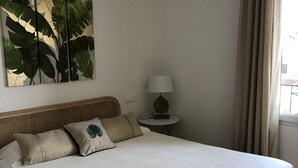 A neatly made bed with a white comforter and two pillows, a wall-mounted plant, a bedside lamp, and a window with curtains. - Hotel Santa Lucia (Saint-Raphael)
