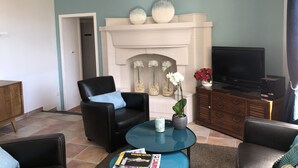 A living room with a fireplace, a television, and a coffee table with magazines. - Hotel Santa Lucia (Saint-Raphael)