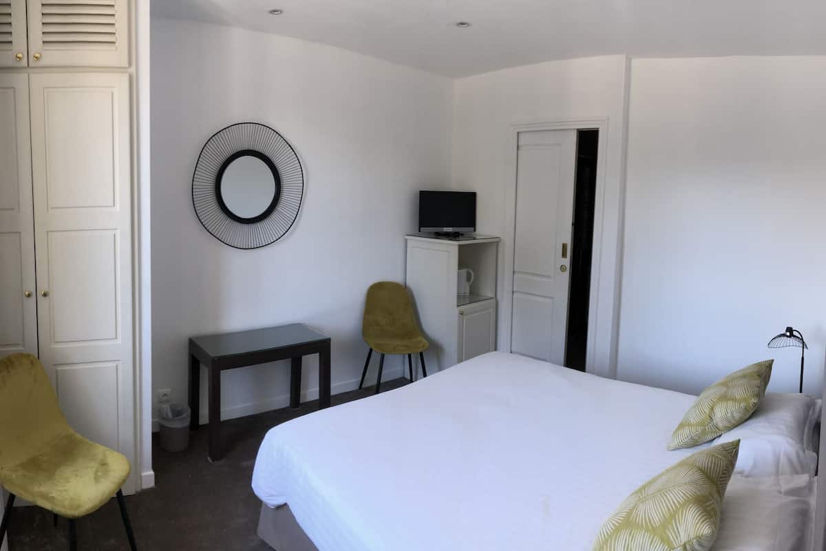 A hotel room with a bed, a desk, a chair, a TV, and a wardrobe.