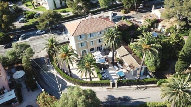 An aerial view of a two-story building with a tiled roof, surrounded by palm trees and a swimming pool. - Hotel Santa Lucia (Saint-Raphael)