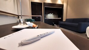 A hotel room with a dining table, a glass of water, a plate with a snack, a pen, and a couch. - JOIVY Spadari (Milan)