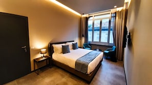 Een hotelkamer met een bed, nachtkastje, lamp en uitzicht op de stad door het raam.