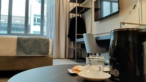 A modern hotel room with a sofa, a dining table with a plate, two glasses, and a coffee maker. - JOIVY Spadari (Milan)