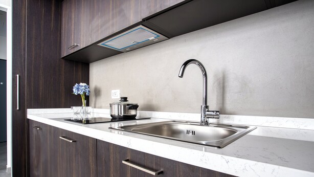 Una cocina moderna con armarios de madera oscura, un lavamanos de acero inoxidable y una encimera de mármol.