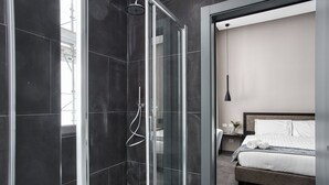 Un baño moderno con ducha de vidrio, una cama grande con ropa blanca y un diseño minimalista.