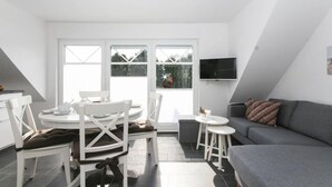A modern, well-lit room with a dining table, chairs, a sofa, and a TV mounted on the wall. - Adams Kajüte (Krummhoern)