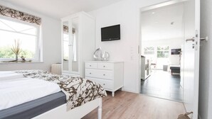 A modern bedroom with a bed, a dresser, a TV, and a view of the living area. - Adams Kajüte (Krummhoern)