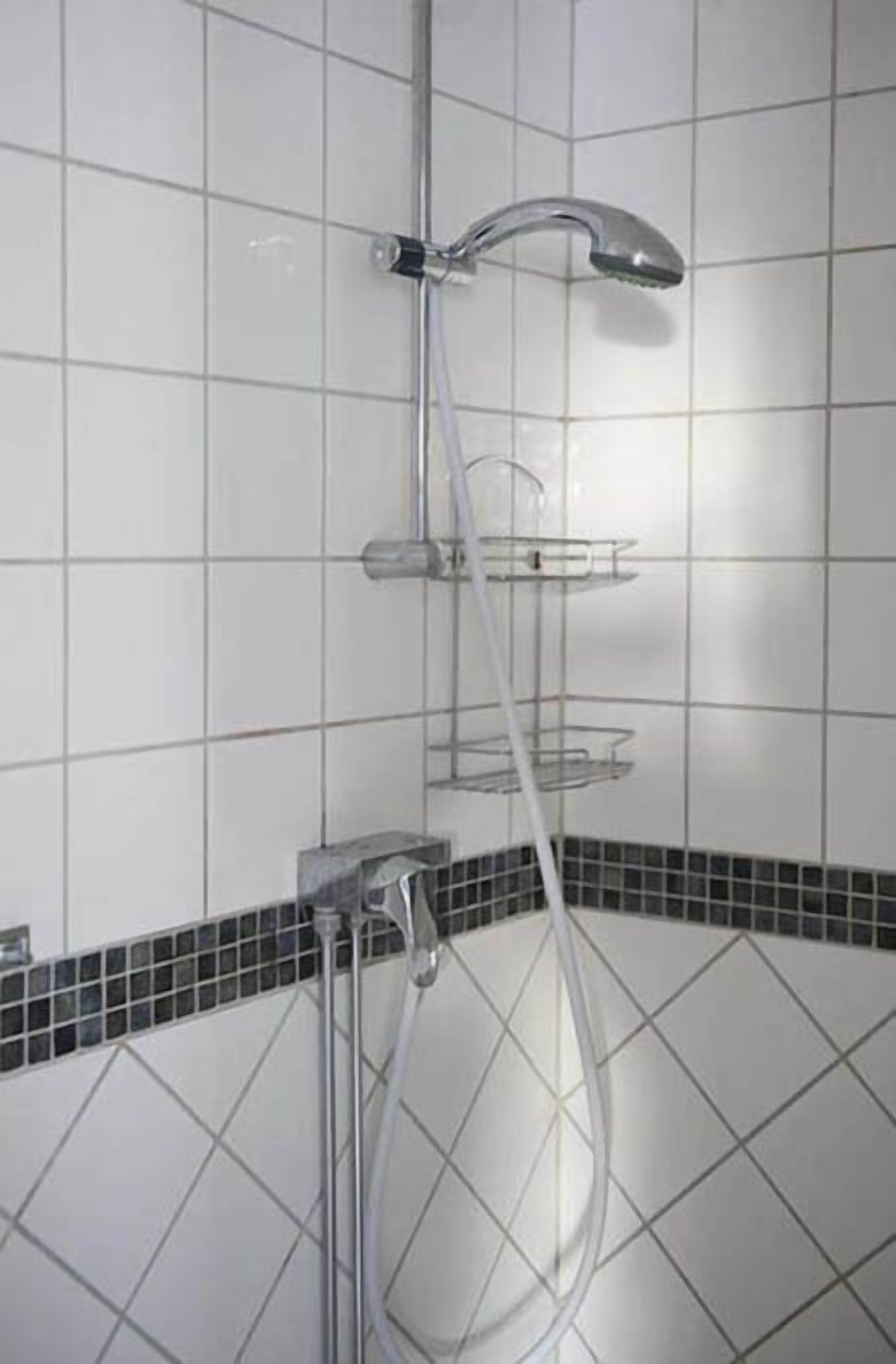 En dusch med ett kromfärgat blandare och en vit kakelbeklädd vägg.