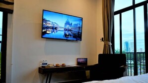 Une chambre d’hôtel avec un lit, un bureau avec un ordinateur portable, un téléviseur diffusant une vue sur la ville et une fenêtre donnant sur des immeubles.
