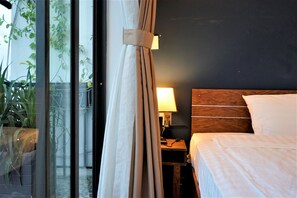 Een hotelkamer met een bed, nachtkastje met lamp, houten hoofdeinde en uitzicht op groen.