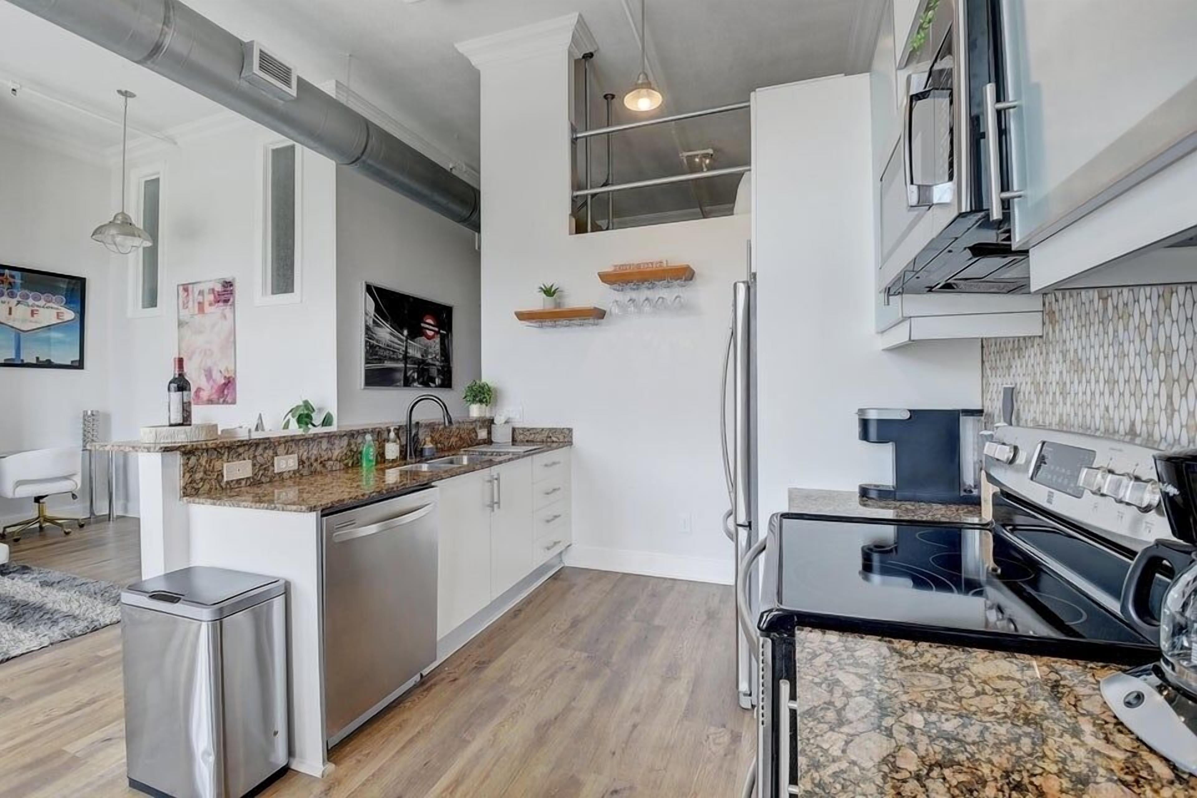 A modern kitchen with stainless steel appliances, a granite countertop, and a small trash bin.