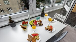 A breakfast table with various foods and drinks, a potted plant, and a view of the outside through a window. - Warsaw Concierge Silver Apartment (Warsaw)