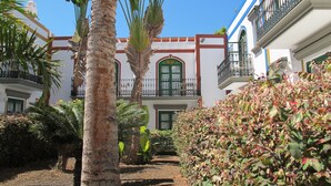 A courtyard with palm trees, a pathway, and a building with balconies and arched windows. - Playa De Mogan Miramar (Mogan)