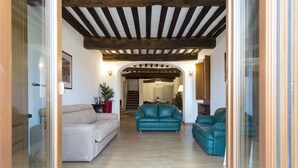 A spacious living room with a wooden ceiling, a beige sofa, and two teal armchairs. - Palazzo Piccolomini (Siena)