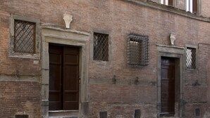 A brick building with two large wooden doors and multiple windows with metal grilles. - Palazzo Piccolomini (Siena)