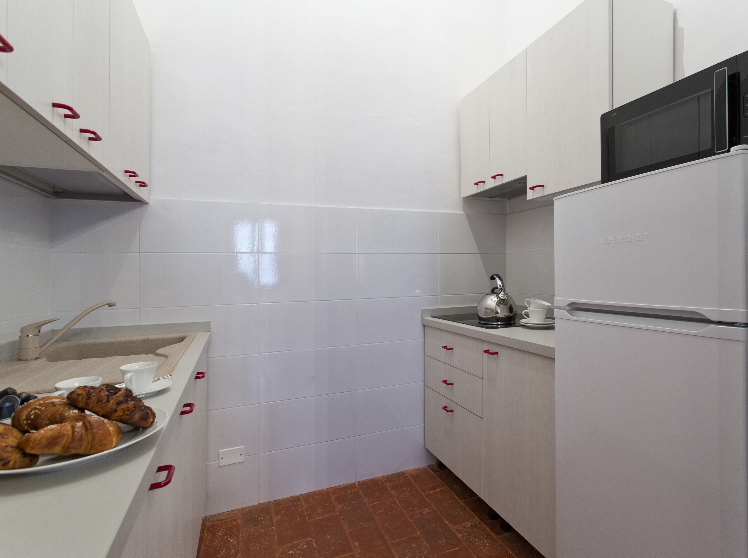 A modern kitchen with white cabinets, a stainless steel kettle, and a microwave.