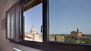 A window with a view of a cityscape, including a prominent building with a dome and another with a bell tower. - Palazzo Piccolomini (Siena)
