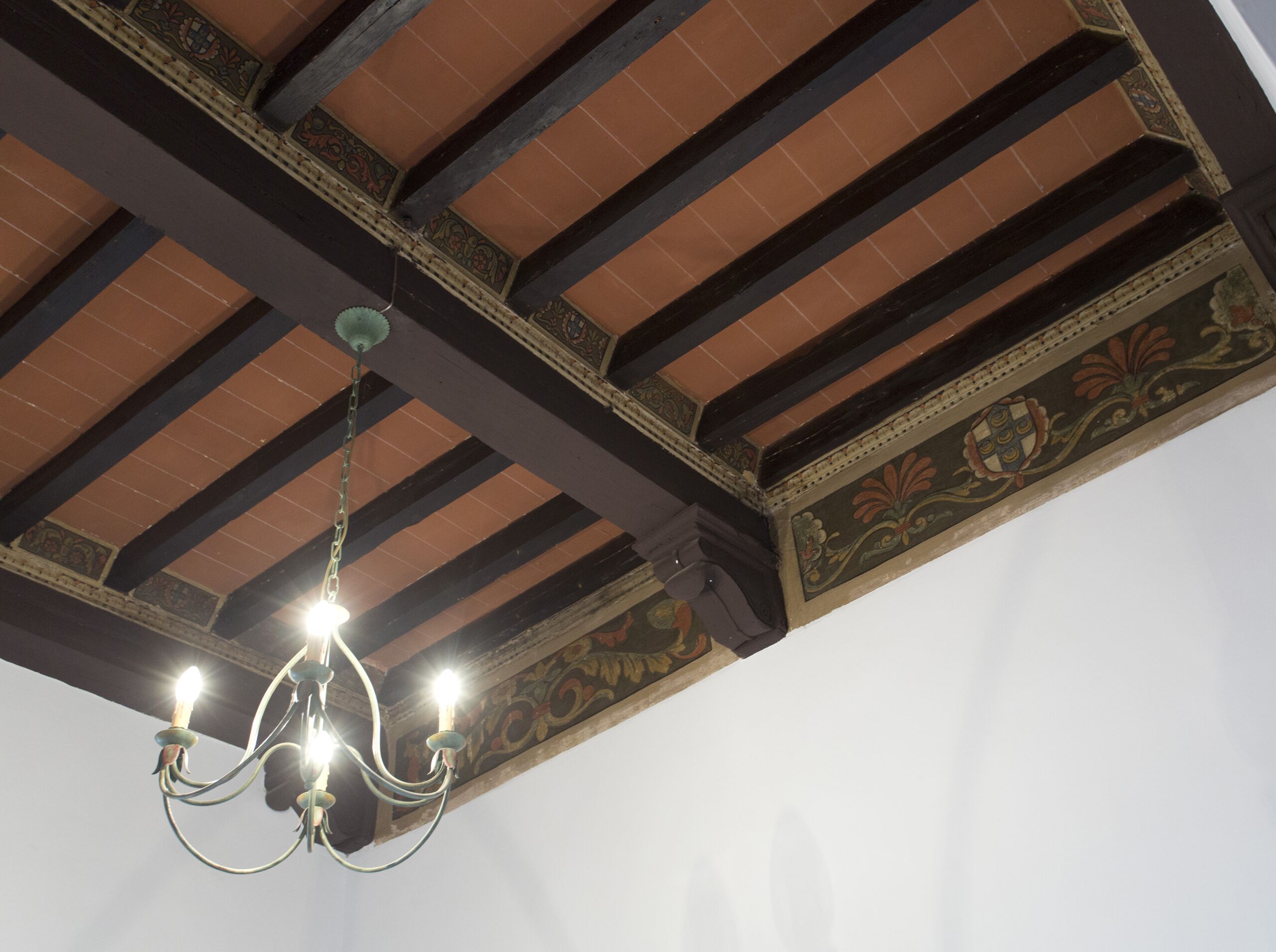 A ceiling with exposed wooden beams and ornate tile work.
