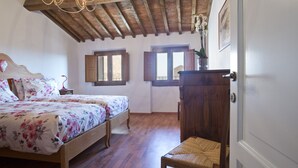 A bedroom with a wooden ceiling, a bed with floral bedding, two windows, and a wooden chair. - Palazzo Piccolomini (Siena)