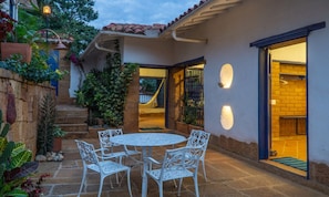 A patio with a round table and chairs, surrounded by plants and a stone wall.