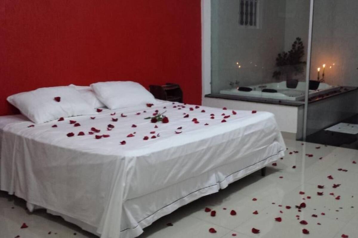 Une chambre à coucher avec un lit recouvert de pétales de roses, une cloison en verre, une petite table avec des bougies et un mur rouge.