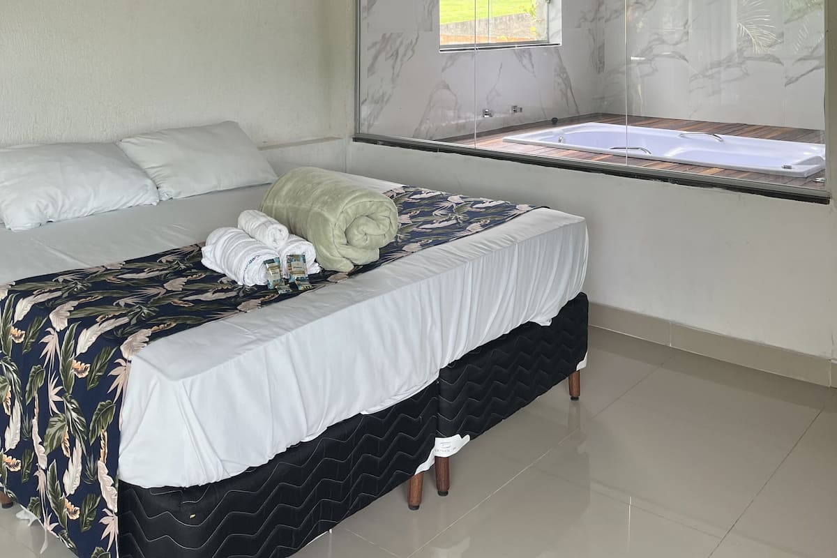 Une chambre à coucher avec un lit, un grand miroir, une fenêtre et une baignoire intégrée.