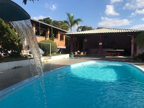 A swimming pool with a waterfall feature, surrounded by a covered patio area with outdoor seating. - Pousada Cantim de BH (Belo Horizonte)