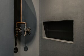 Um quarto com uma parede escura, uma janela com moldura branca e um cano com uma válvula.