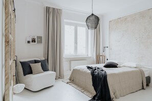 Quarto minimalista com cama, uma cadeira, luminária pendente e janela.