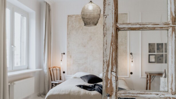 A bedroom with a bed, a chair, a hanging light fixture, and a mirror. - Warsaw Concierge Unique Design Studio (Warsaw)