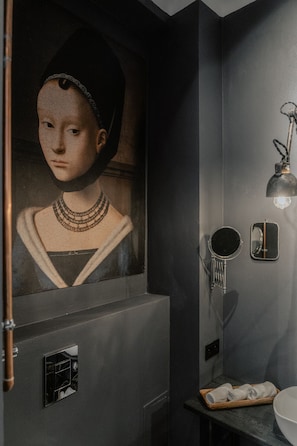 Um banheiro com um retrato em estilo renascentista, um espelho, um lustre e um porta-toalhas.