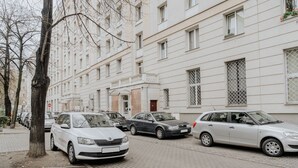 A row of parked cars along a sidewalk in front of a white building with multiple windows and balconies. - Warsaw Concierge Unique Design Studio (Warsaw)